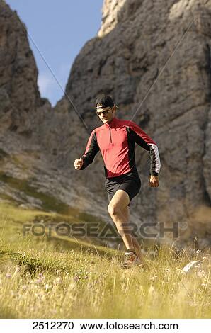 Stock Image - Mid adult man running on landscape, Trentino-Alto Adige, Italy . Fotosearch