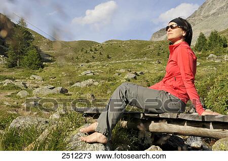 Stock Image - Mid adult woman sitting on footbridge, Trentino-Alto Adige, Italy . Fotosearch