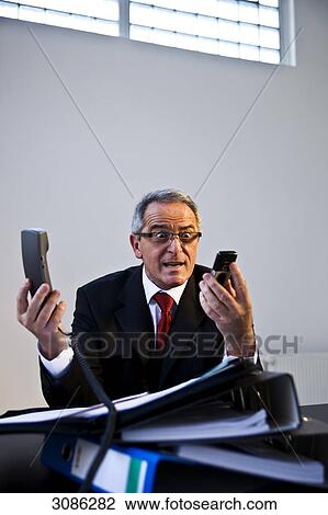 Overworked businessman holding two telephones View Large Photo Image Stock Image - Overworked businessman holding two telephones . Fotosearch