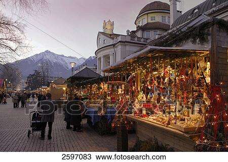 Stock Image - People at market stalls lit up at dusk, Trentino-Alto Adige, Italy . Fotosearch