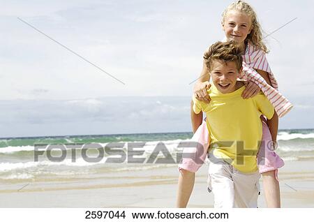 Portrait of boy giving a piggyback ride to his sister on the beach View Large Photo Image Picture - Portrait of boy giving a piggyback ride to his sister on the beach . Fotosearch