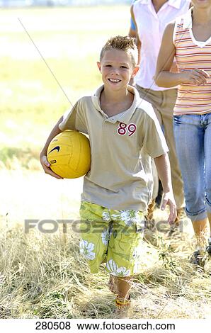 Stock Photo - Portrait of boy holding ball and walking in field . Fotosearch