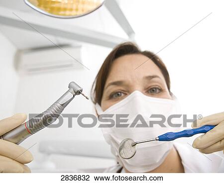 Stock Image - Portrait of female dentist holding dental drill and angled mirror . Fotosearch