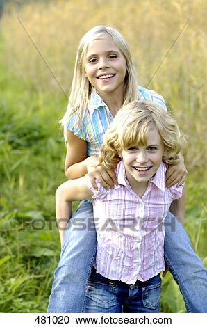 Portrait of girl giving her sister a piggyback ride in a field View Large Photo Image Stock Image - Portrait of girl giving her sister a piggyback ride in a field . Fotosearch