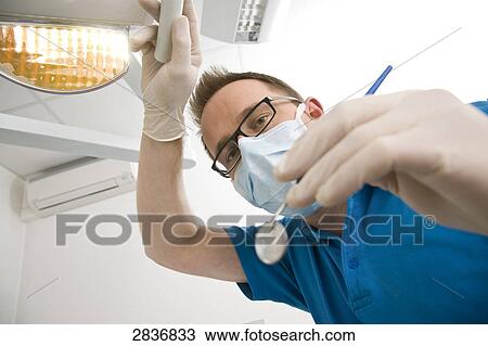 Stock Image - Portrait of male dentist holding angled mirror . Fotosearch