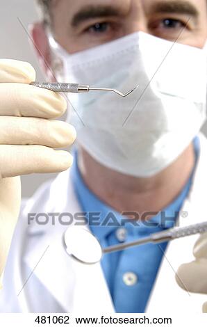 Stock Image - Portrait of male dentist holding plaque remover and angled mirror . Fotosearch