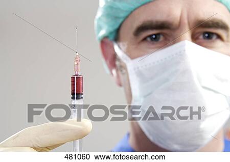 Stock Image - Portrait of male surgeon holding syringe . Fotosearch
