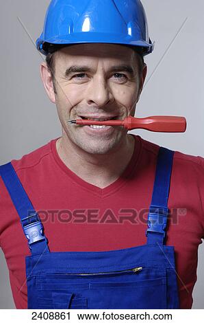 Stock Image - Portrait of man holding screwdriver in his mouth . Fotosearch
