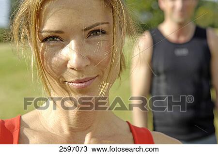 Stock Image - Portrait of young woman smiling with man standing in background . Fotosearch