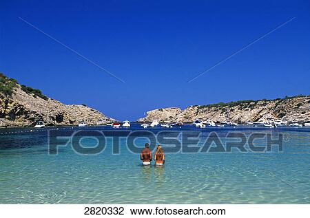 Stock Image - Rear view of couple standing in shallow water, Cala Moli, Ibiza, Balearic Islands, Spain . Fotosearch