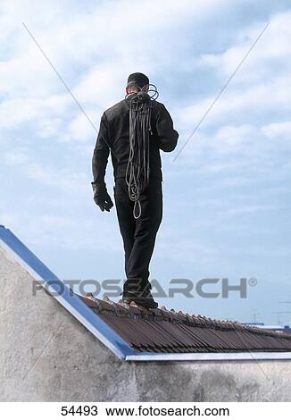 Stock Image - Rear view of man walking on roof . Fotosearch