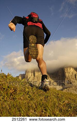 Stock Image - Rear view of mid adult man running on landscape, Trentino-Alto Adige, Italy . Fotosearch