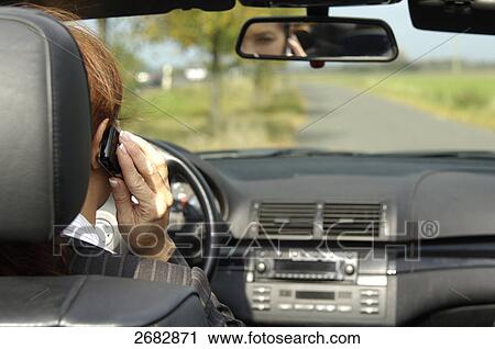 Stock Image - Rear view of woman talking on mobile phone while driving car . Fotosearch