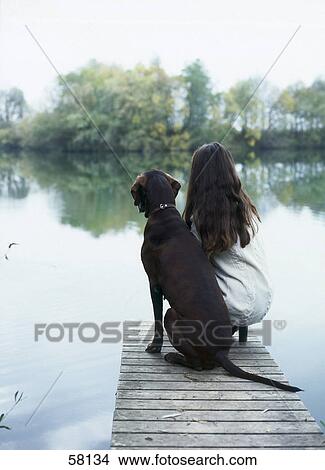 Rear view of young woman sitting with dog on pier View Large Photo Image Picture - Rear view of young woman sitting with dog on pier . Fotosearch