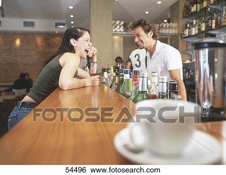 Stock Photograph - Side profile of young woman and bartender laughing at bar counter . Fotosearch