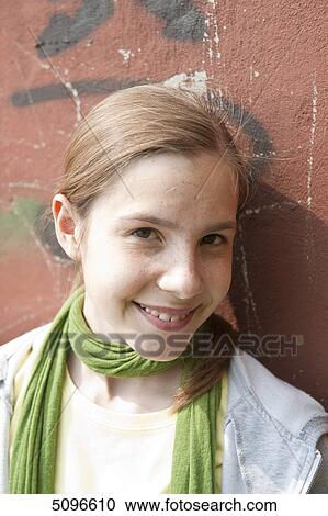 Stock Image - Smiling girl leaning at wall, portrait . Fotosearch