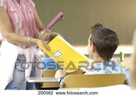 Stock Image - Teacher giving exercise book to boy in classroom . Fotosearch