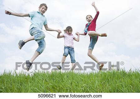 Three children jumping hand in hand in meadow View Large Photo Image Stock Image - Three children jumping hand in hand in meadow . Fotosearch