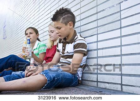 Three children sitting on the ground and holding bottles of alcohol, low angle view View Large Photo Image Stock Photograph - Three children sitting on the ground and holding bottles of alcohol, low angle view . Fotosearch