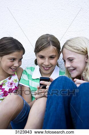 Stock Image - Three girls looking at a mobile phone . Fotosearch