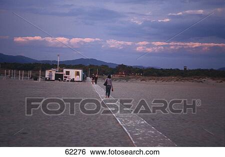 Stock Photograph - Three people on walkway at beach, beach evening light, Apuan Alps, Viareggio, Tuscany, Italy . Fotosearch