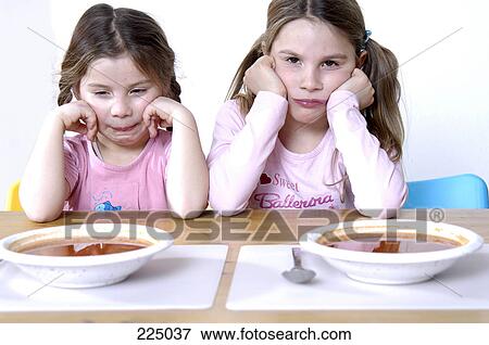 Two girls looking displeased at the breakfast table View Large Photo Image Stock Photo - Two girls looking displeased at the breakfast table . Fotosearch