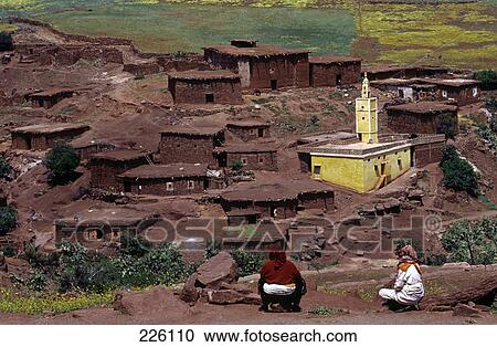 Stock Image - Two women sitting on hill overlooking village, Morocco . Fotosearch