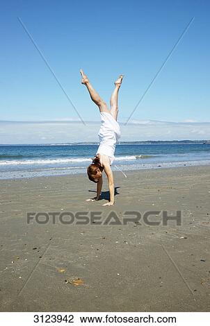 Stock Image - Woman doing a handstand on a beach . Fotosearch