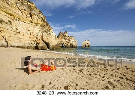 Stock Photo - Woman lying at beach, Praia dos Tres Irmaos, Algarve, Portugal . Fotosearch