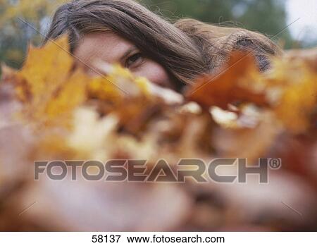 Stock Photo - Woman lying on ground and looking through leaves . Fotosearch
