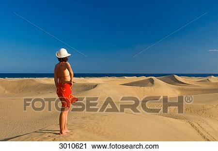 Stock Image - Woman standing on a sand dune looking at the sea, Maspalomas, Gran Canaria, Spain, rear view . Fotosearch