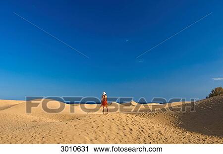 Stock Image - Woman standing on a sand dune, Maspalomas, Gran Canaria, Spain, rear view . Fotosearch