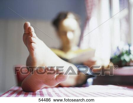 Stock Photograph - Woman with feet on table reading a book, blurred . Fotosearch