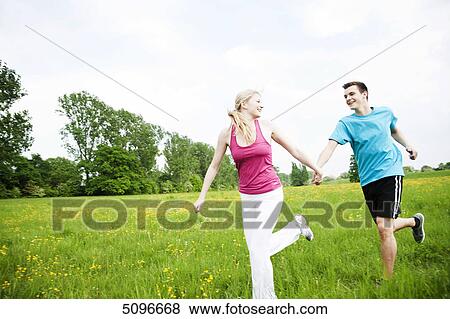 Stock Photo - Young couple running in meadow hand in hand . Fotosearch