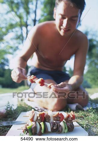Stock Image - Young man preparing kebab during picnic . Fotosearch