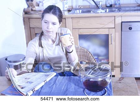 Stock Image - Young woman having breakfast in kitchen . Fotosearch