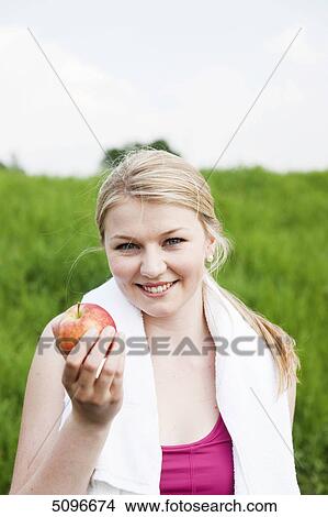 Young woman holding apple outdoors, portrait View Large Photo Image Picture - Young woman holding apple outdoors, portrait . Fotosearch
