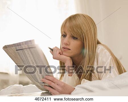 Stock Image - Young woman lying with newspaper in bed . Fotosearch