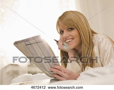 Stock Image - Young woman lying with newspaper in bed . Fotosearch