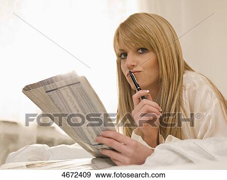Stock Photo - Young woman lying with newspaper in bed . Fotosearch