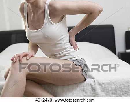 Stock Image - Young woman sitting on bed . Fotosearch