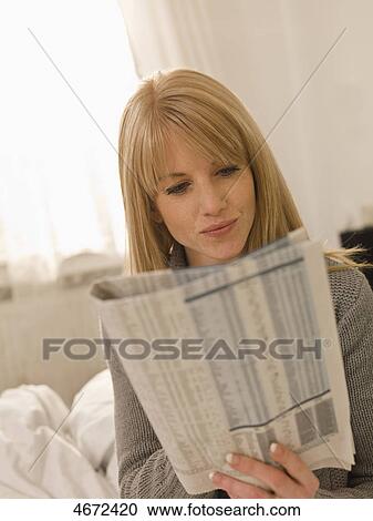 Stock Image - Young woman with newspaper in bed . Fotosearch