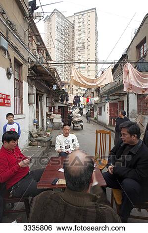Stock Photograph - Man sitting around a table in a working class are, new building in the background, Shanghai, China . Fotosearch