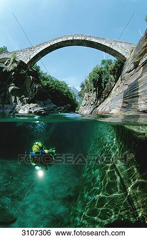 Stock Photograph - Scuba diver in the Verzasca river with stone bridge in the background, Tessin, Switzerland, underwater shot . Fotosearch