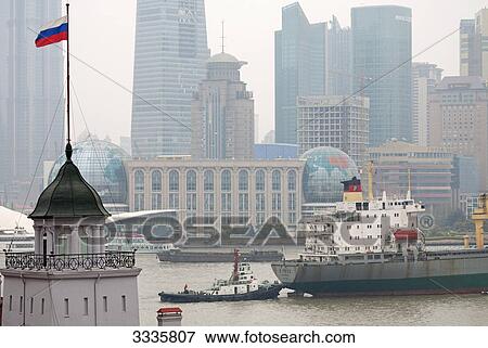Stock Photo - Ship and tugboat on a Huangpu River, Skyscrapers in the background, Shanghai, China, elevated view . Fotosearch