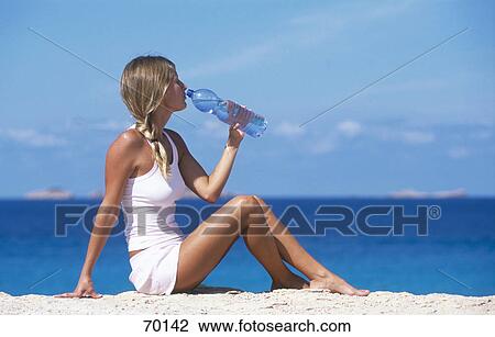 Stock Image - Side profile of young woman drinking water from bottle on beach . Fotosearch