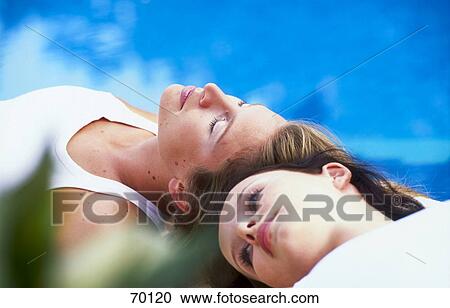 Two young women resting on a poolside View Large Photo Image Stock Image - Two young women resting on a poolside . Fotosearch