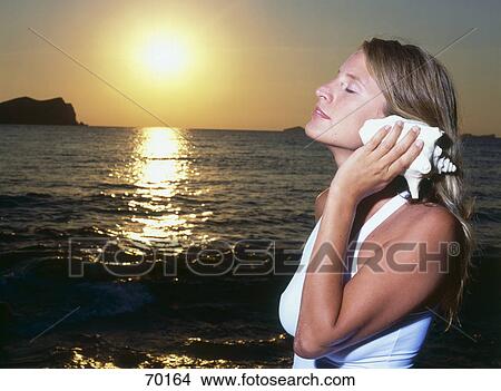 Young woman listening to shell View Large Photo Image Picture - Young woman listening to shell . Fotosearch
