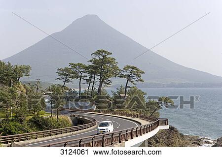 Stock Image - Car on a coastal road, volcano in the background, Ibusuki, Kyushu, Japan . Fotosearch