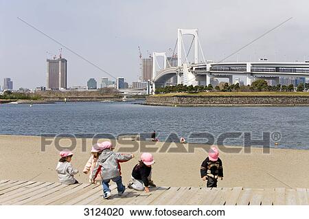 Stock Image - Children playing at a river shore, Rainbow bridge in the background, Tokyo, Japan . Fotosearch